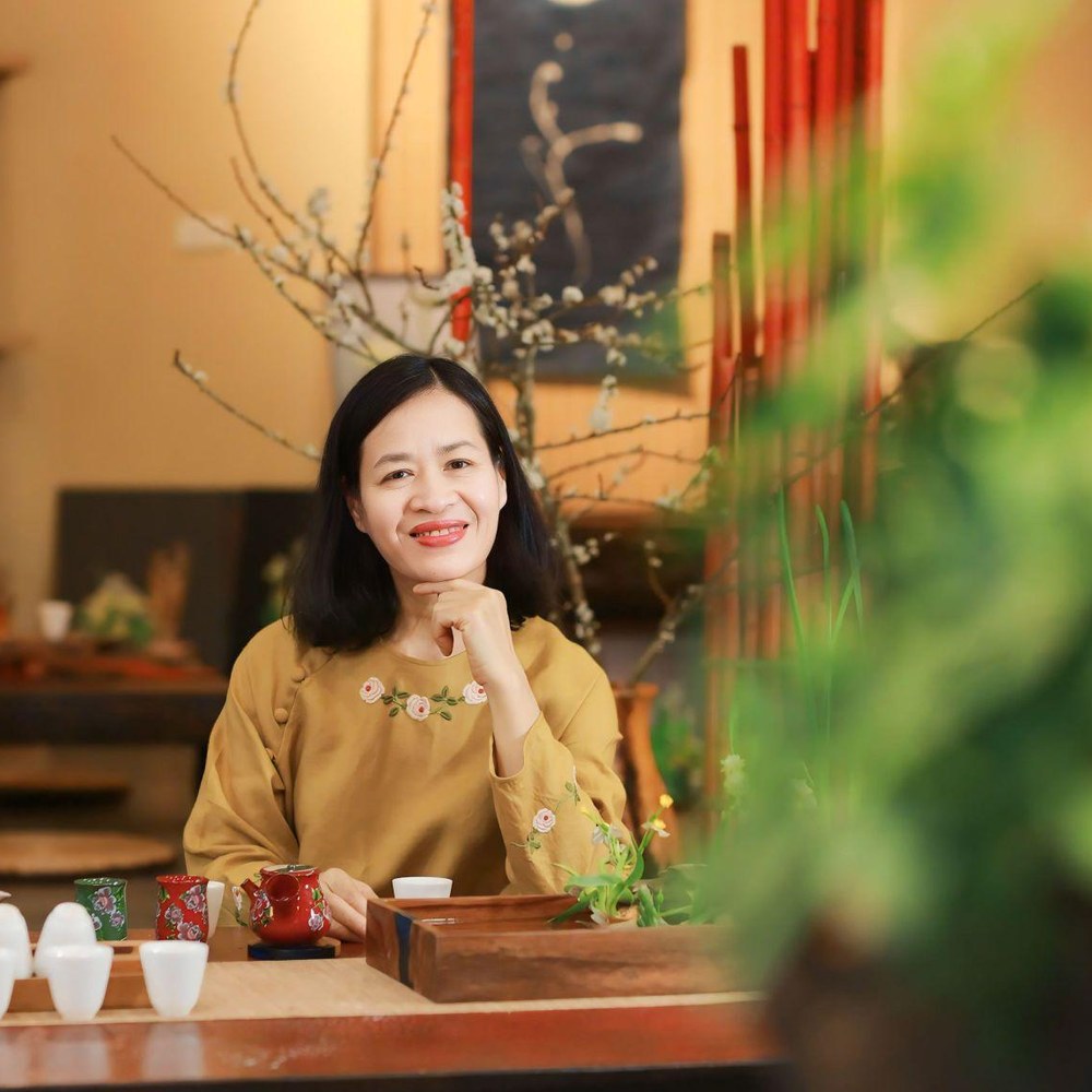 Coach Hồng Nga, chân dung gần, ánh mắt hướng về phía người xem, không gian ấm áp có cây xanh